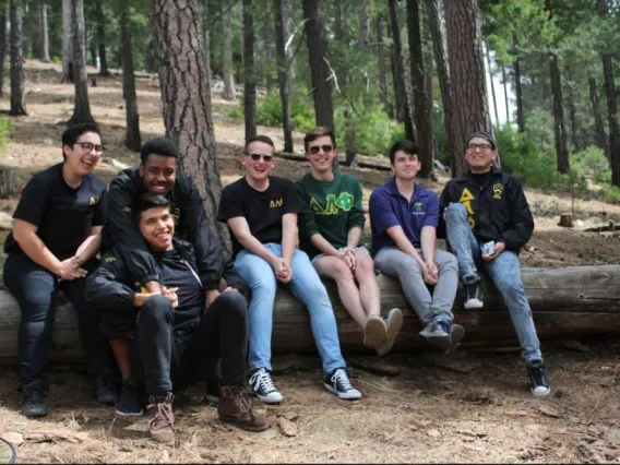 Delta Lambda Phi Omega Chapter members sitting on tree laughing