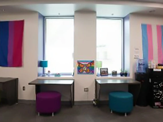 Small desks sitting under windows with colorful stools