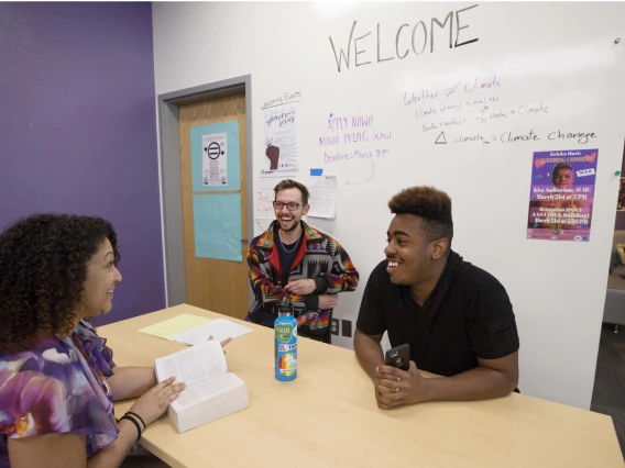 Students smiling and laughing while conducting a meeting, ideas written on a white board in the background