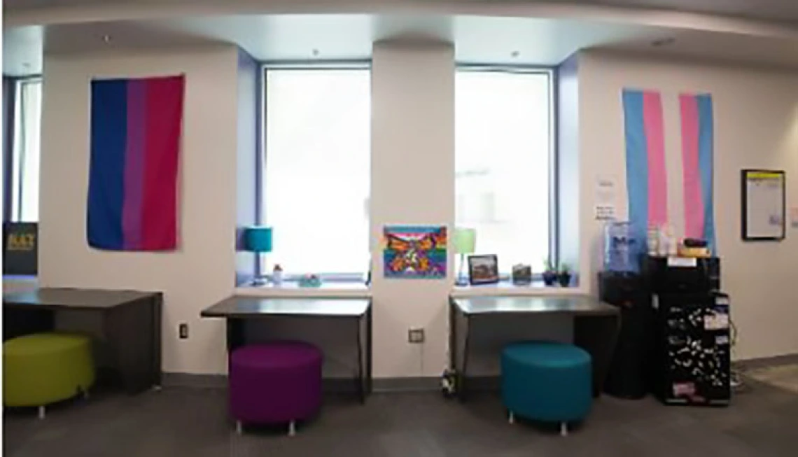 Small desks sitting under windows with colorful stools