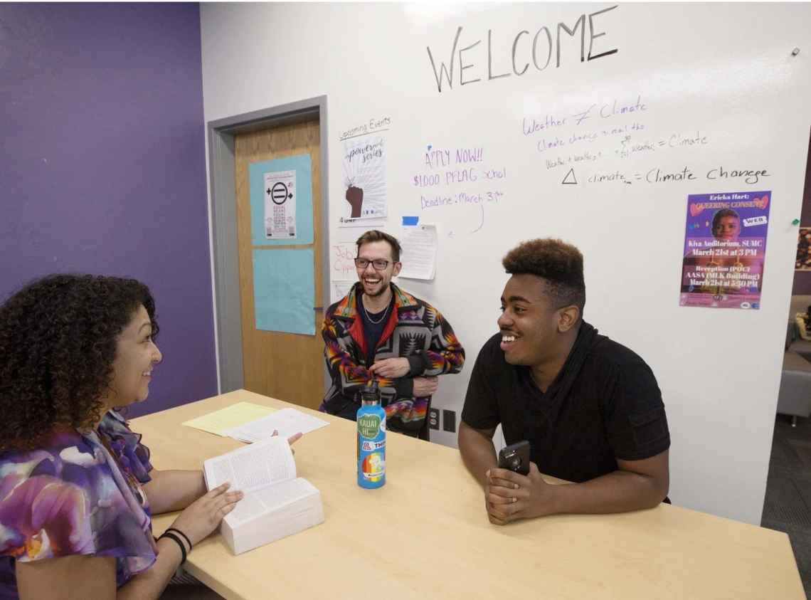 Students smiling and laughing while conducting a meeting, ideas written on a white board in the background