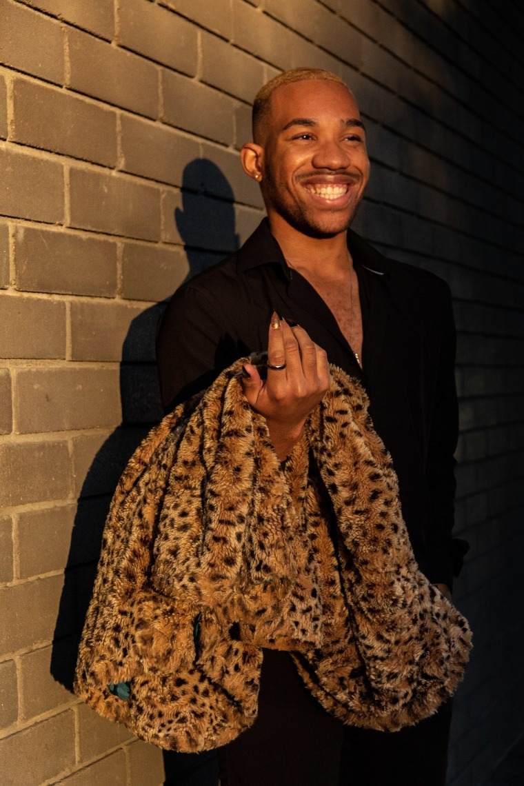 Daijon stands in dramatic lighting from the left, holding a leopard print coat draped over his arm