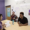 Students smiling and laughing while conducting a meeting, ideas written on a white board in the background